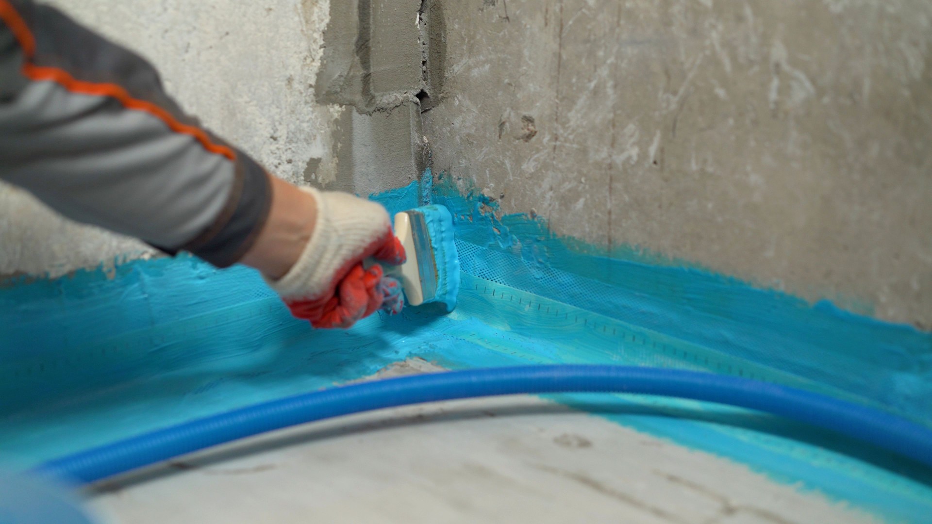 Construction worker waterproofing bathroom corner using blue liquid membrane and sealing tape, ensuring protection against leaks and moisture